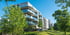 Moderne Wohngebäude mit Balkonen, umgeben von grünen Bäumen und Rasenflächen unter blauem Himmel.