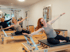 Drei Frauen trainieren mit ausgestreckten Armen auf Pilates-Reformern in einem hellen Studio.