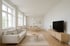 Modernes, minimalistisches Wohnzimmer mit hellem Sofa, Holztisch, Esstischgruppe und großem Fernseher.