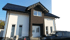 Modernes Einfamilienhaus mit weißer Fassade, dunklem Klinker-Mittelbau, schwarzem Satteldach und davor parkendem schwarzem PKW.