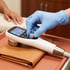 A gloved hand adjusts the dial on a handheld medical ultrasound device with a digital display screen.