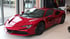 Roter Ferrari Sportwagen mit "KFZ Sachverständiger" Logo auf der Seite, in einem Ausstellungsraum.