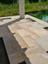 Terrasse aus beigen Natursteinplatten an einem Schwimmteich mit Schilfbepflanzung im Hintergrund.