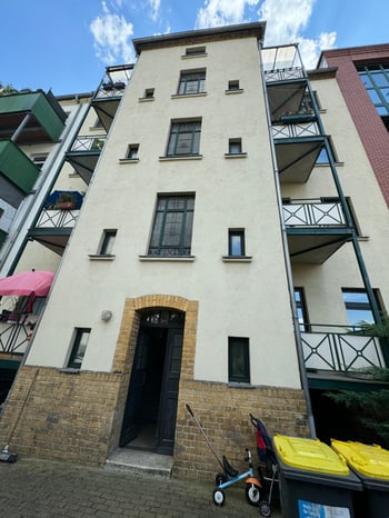 Hofseite des Gebäudes mit grün gestrichenen Balkonen und Mülltonnen im Eingangsbereich