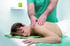 Physiotherapeut massiert den Schulterbereich einer liegenden Frau in einer Praxis.