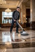 Ein Mann in Arbeitskleidung poliert einen glänzenden Marmorboden in einer luxuriösen Hotellobby mit einer Bodenpoliermaschine.