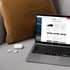 Laptop auf Sofa zeigt Website zur Busauswahl, daneben weiße kabellose Kopfhörer.