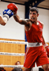 Ein Boxer in roter Kleidung und roten Handschuhen schlägt mit der rechten Faust zu und trägt einen Mundschutz.