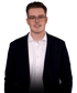Lachender junger Mann mit Brille, weißem Hemd und dunklem Sakko.