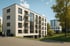 Modernes weißes Mehrfamilienhaus mit orangen Fensterläden, Balkonen und Tiefgarageneinfahrt, umgeben von Bäumen.