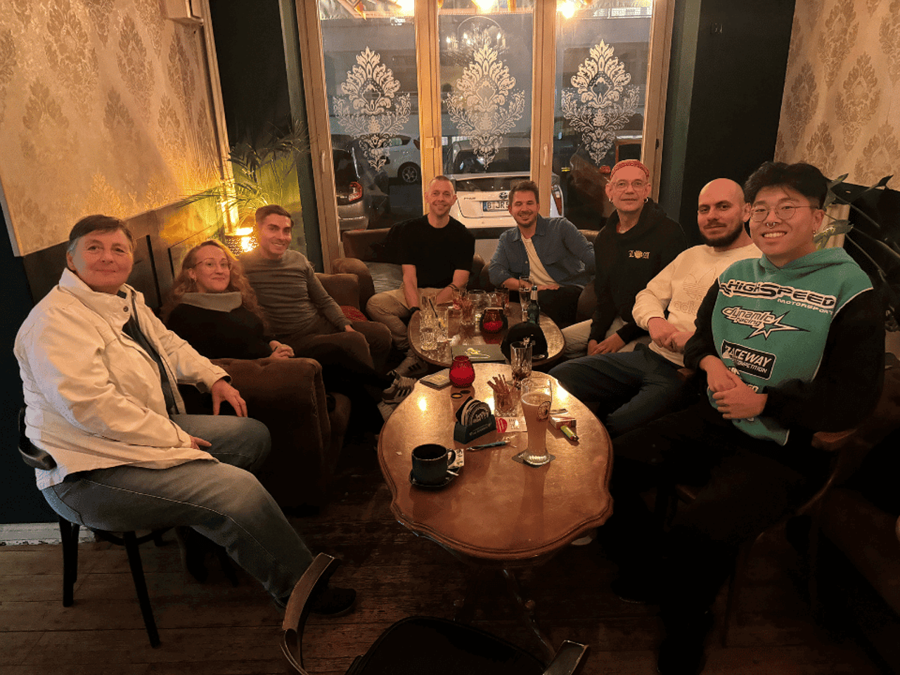 A group of eight people sit in a cozy bar around two wooden tables.