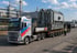 Ein Volvo-LKW von Gutmann Transport befördert eine schwere Industriekomponente auf einem Tieflader vor einem Fabrikgelände.