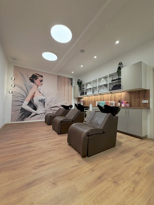 Friseursalon mit braunen Waschsesseln, Holzfußboden und einer Wandtapete mit einer Frau in einem Federkleid.