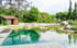 Moderner Schwimmteich mit Holzsteg, kleiner Brücke, Gartenhaus und grüner Uferbepflanzung.