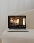 Laptop auf einem cremefarbenen Hocker zeigt die Webseite "DAS PFEIFFERS" mit Restaurant-Interieur.