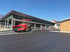 Roter Straßenfertiger asphaltiert eine Fläche vor einem großen Stallgebäude unter blauem Himmel.