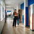 Teacher and student review papers in a bright school hallway with blue and orange accents.