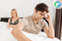 A man sits on a bed with his head in his hand, facing erectile dysfunction, while a woman with crossed arms sits behind him