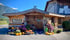 Holzhütte "Steirer's Hofladele" mit Kürbissen und Blumen unter einem Holzhahn-Schild. bauernhof paznaun, bauernhof tirol, martalas hof, christoph ladner, christine ladner, regionale produkte tirol, käse tirol kaufen, fleisch vom bauern tirol, hofladen tirol, direktvermarkter tirol, lebensmittel direkt vom bauern
