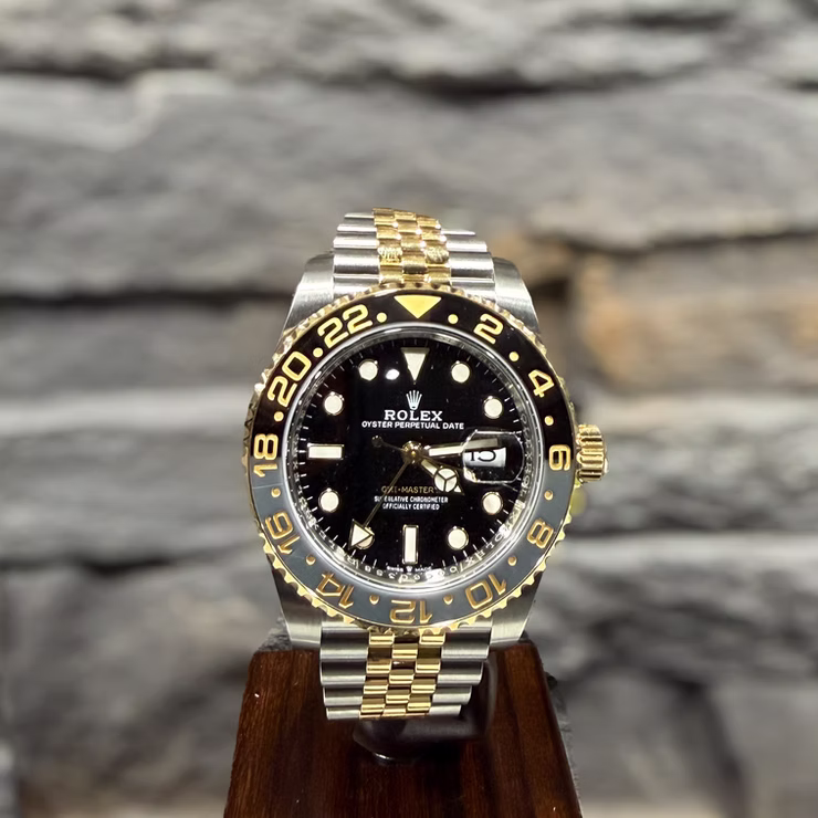 Silberne und goldene Rolex Oyster Perpetual Date GMT-Master Uhr mit schwarzem Zifferblatt auf Holzständer.