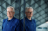 Ein Mann mit Brille und blauem Poloshirt lehnt an einer reflektierenden Glaswand.