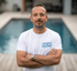 Mann mit Bart und grauem T-Shirt, auf dem "GEIGER Wellness" steht, steht vor einem Pool.