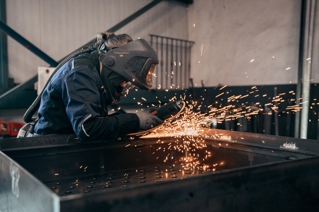 Metallbearbeiter mit Schutzmaske schleift ein Werkstück mit Funkenflug