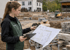 Junge Frau in Arbeitskleidung betrachtet Baupläne auf einer Baustelle mit einem Tablet in der Hand.