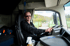 Lachender Lastwagenfahrer mit Sonnenbrille am Steuer eines Lastwagens.