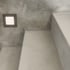 Beleuchteter quadratischer Wandstrahler an einer grauen Betonwand über einer Treppe.