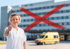 Eine lächelnde Frau in weißer Uniform mit erhobenem Daumen vor einem Krankenhaus mit rotem X und Krankenwagen.