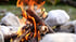 Loderndes Lagerfeuer mit Holzscheiten und Funken, umgeben von großen, hellen Steinen.