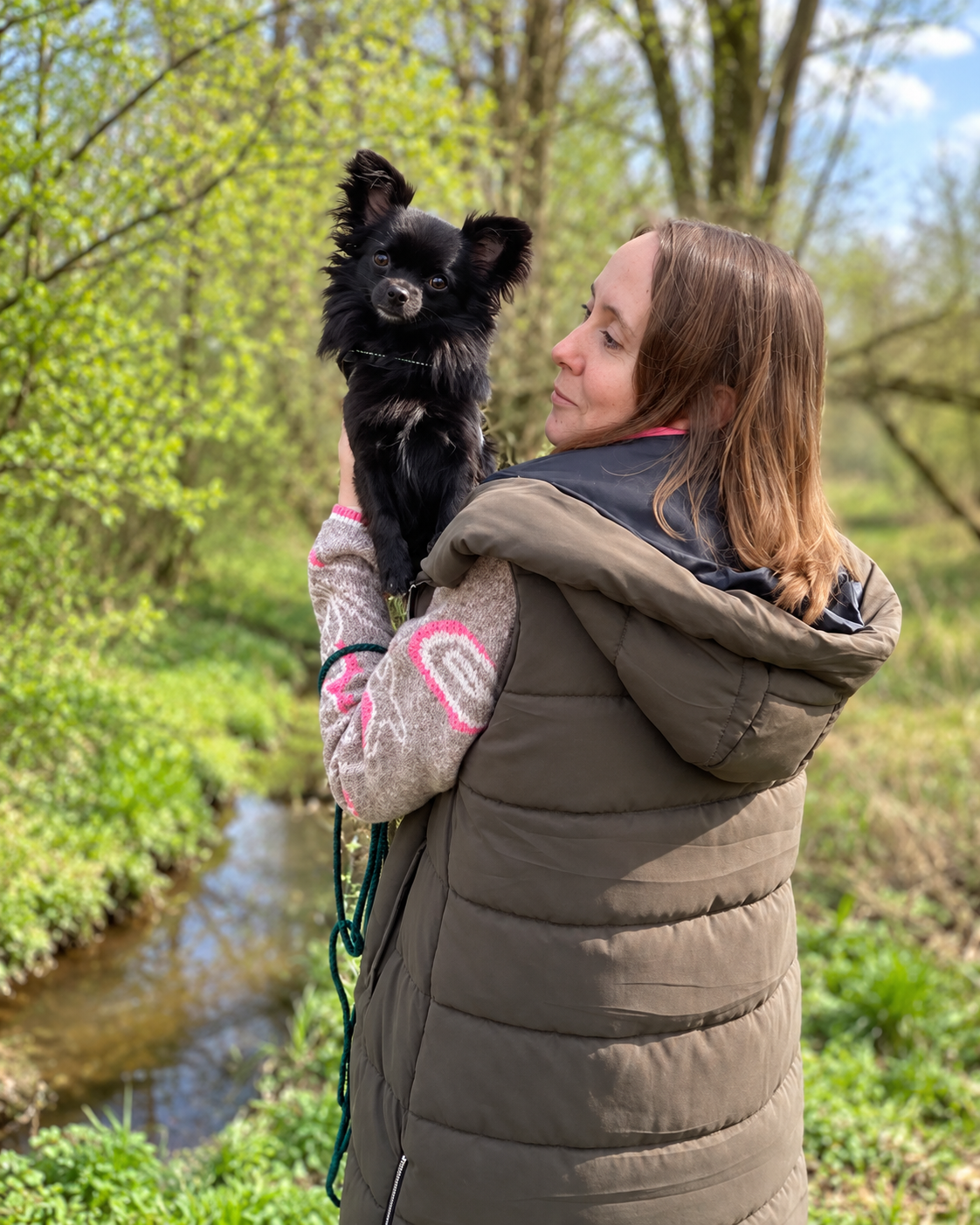 Frau steht mit einem schwarz-weißen Hund auf einer Wiese