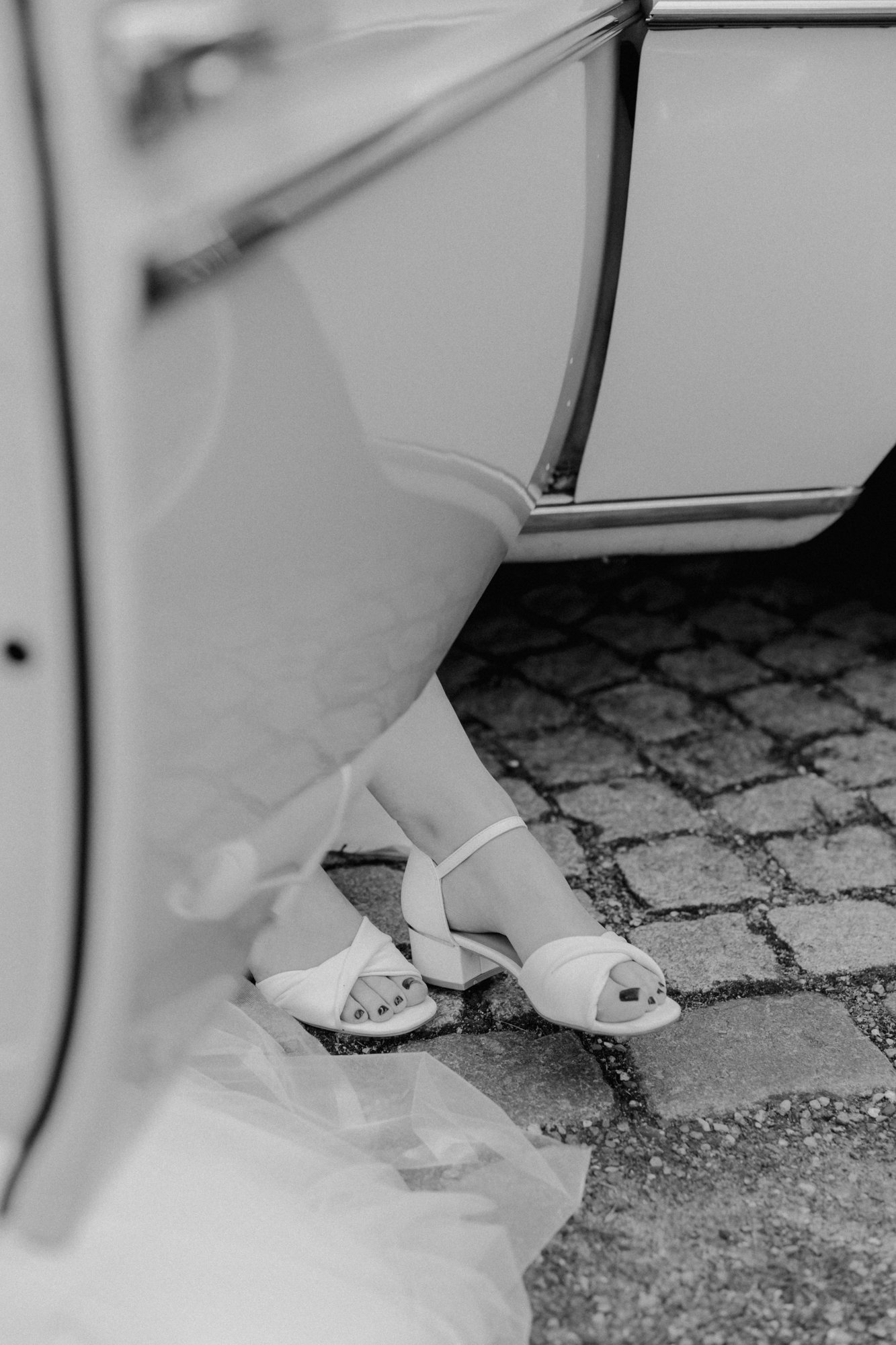 Schwarzweißaufnahme: die Braut steigt aus dem Hochzeitsauto