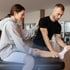 Physical therapist stretches a patient's leg while she sits on an examination table.