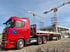 Roter Scania-LKW mit Anhänger und blauen Logos parkt auf einer Baustelle mit zwei Kränen und Rohbau.