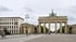 Das Brandenburger Tor in Berlin mit der Quadriga unter bewölktem Himmel am Pariser Platz mit Radfahrern.
