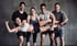 Fünf lachende Fitness-Enthusiasten, die eine Frau in die Höhe heben, die in der Luft liegt.