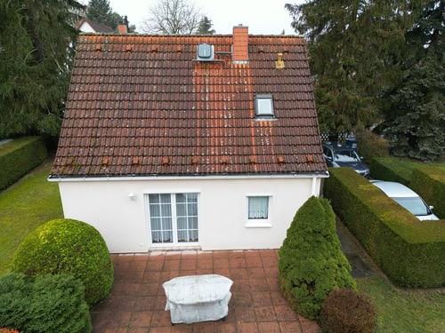 Kleines Haus mit rotem Ziegeldach, weiß gestrichenen Wänden, Terrasse und grüner Hecke.