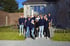 Eine Gruppe von 18 jungen Erwachsenen in dunkelblauen Hoodies und T-Shirts steht vor einem grauen Steinhaus.