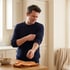 A man in a navy blue sweater rolls up his sleeves while standing in a kitchen next to a bowl of vegetables.