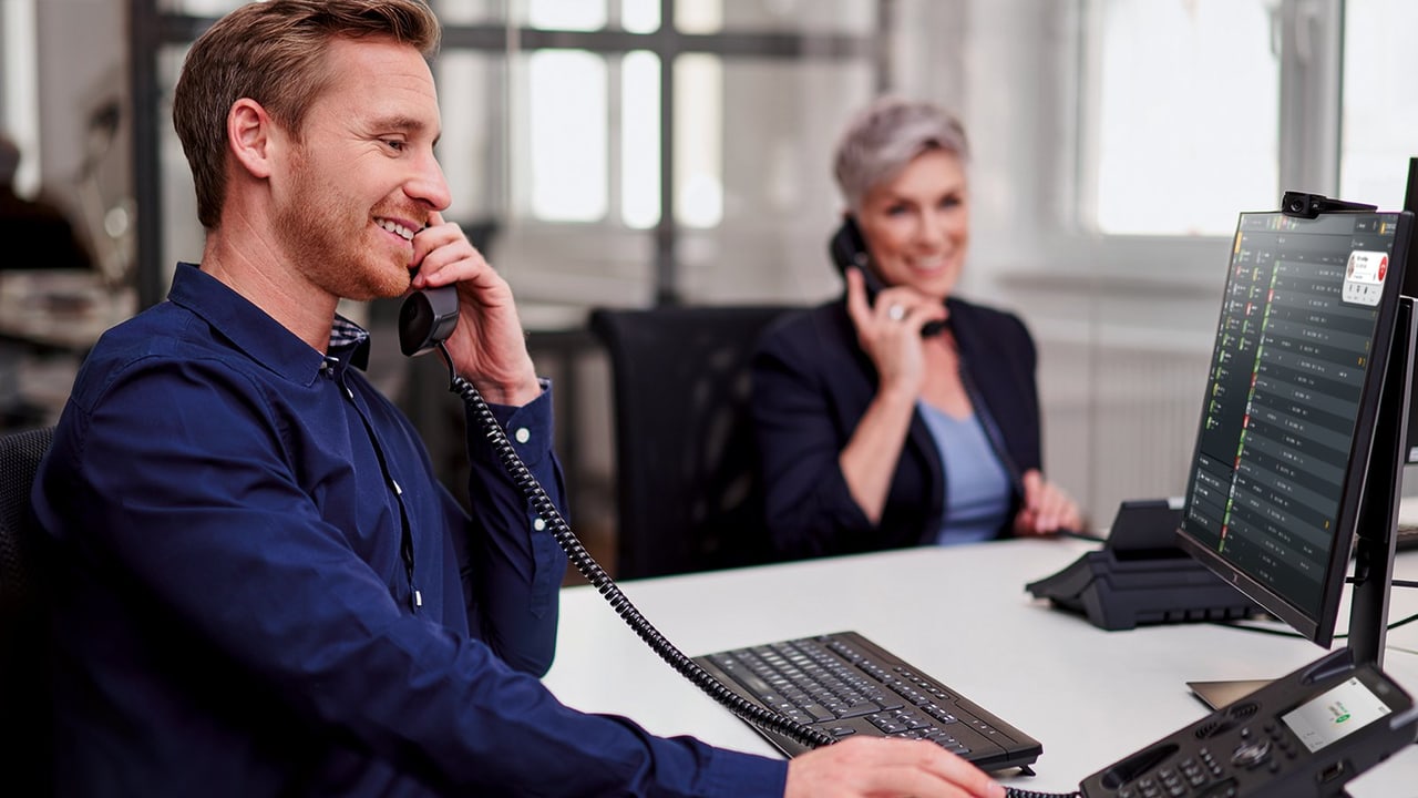 Büro mit zwei Mitarbeitenden am Tischtelefon, auf dem Bildschirm die STARFACE App mit Rufliste