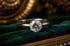 Illustration: Solitärring aus Weißgold mit einem runden Diamanten auf dunkelgrünem Samt, im Hintergrund warme Messingtöne