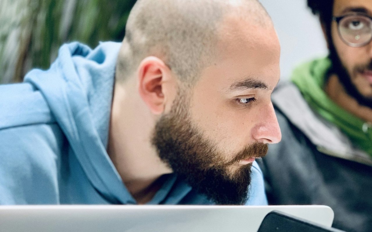 Zwei Männer schauen konzentriert auf den Bildschirm eines MacBooks