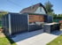 Moderne Outdoor-Küche mit Grill, Spüle, Theke und Barhockern unter einem Dach, umgeben von einem Holzzaun.