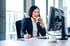 Geschäftsfrau am Schreibtisch telefoniert mit einem Hörer und macht sich Notizen vor einem Computerbildschirm.