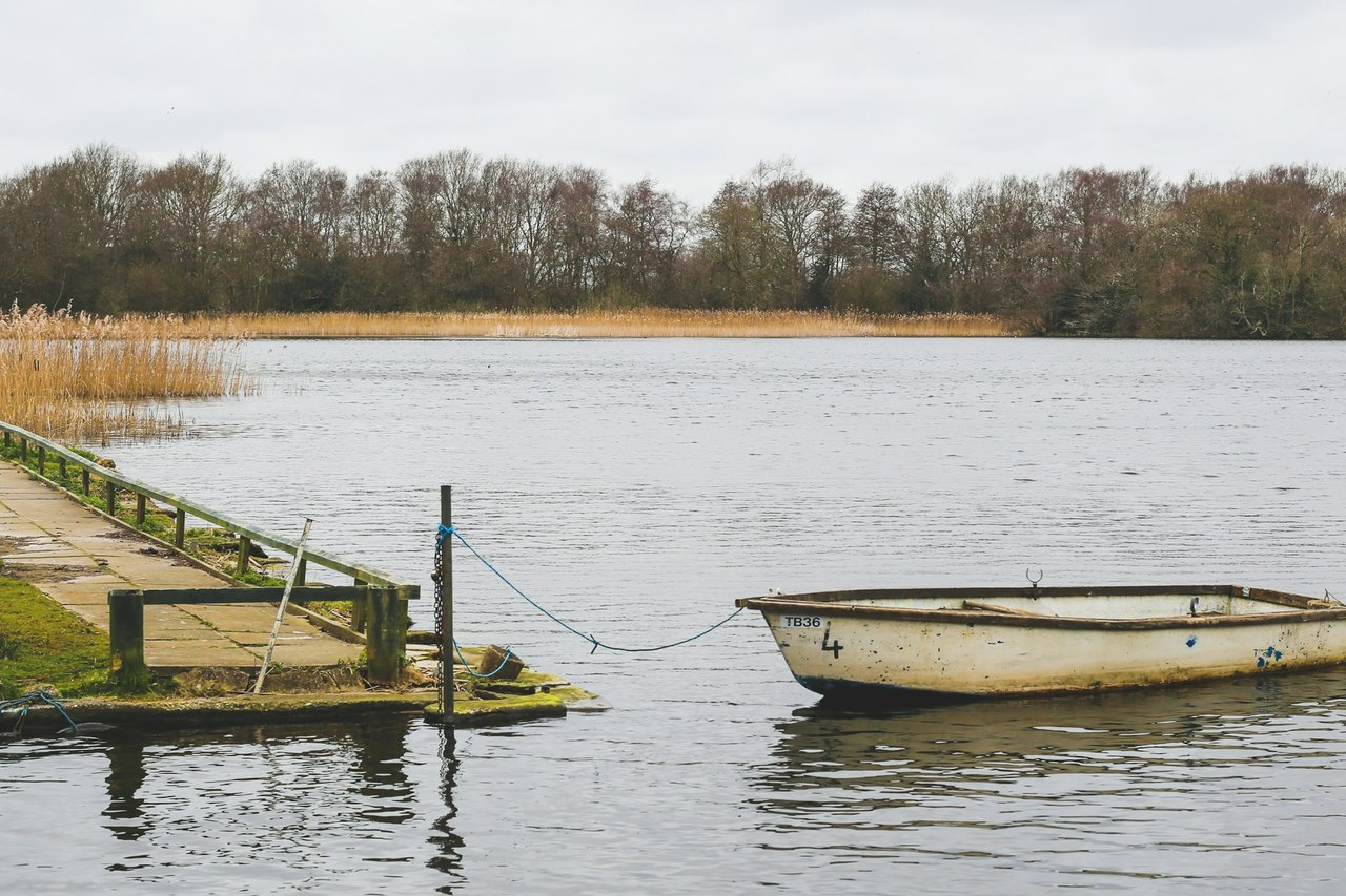 Ein kleines Ruderboot liegt an einem Seil vertäut an einem Steg auf einem ruhigen See