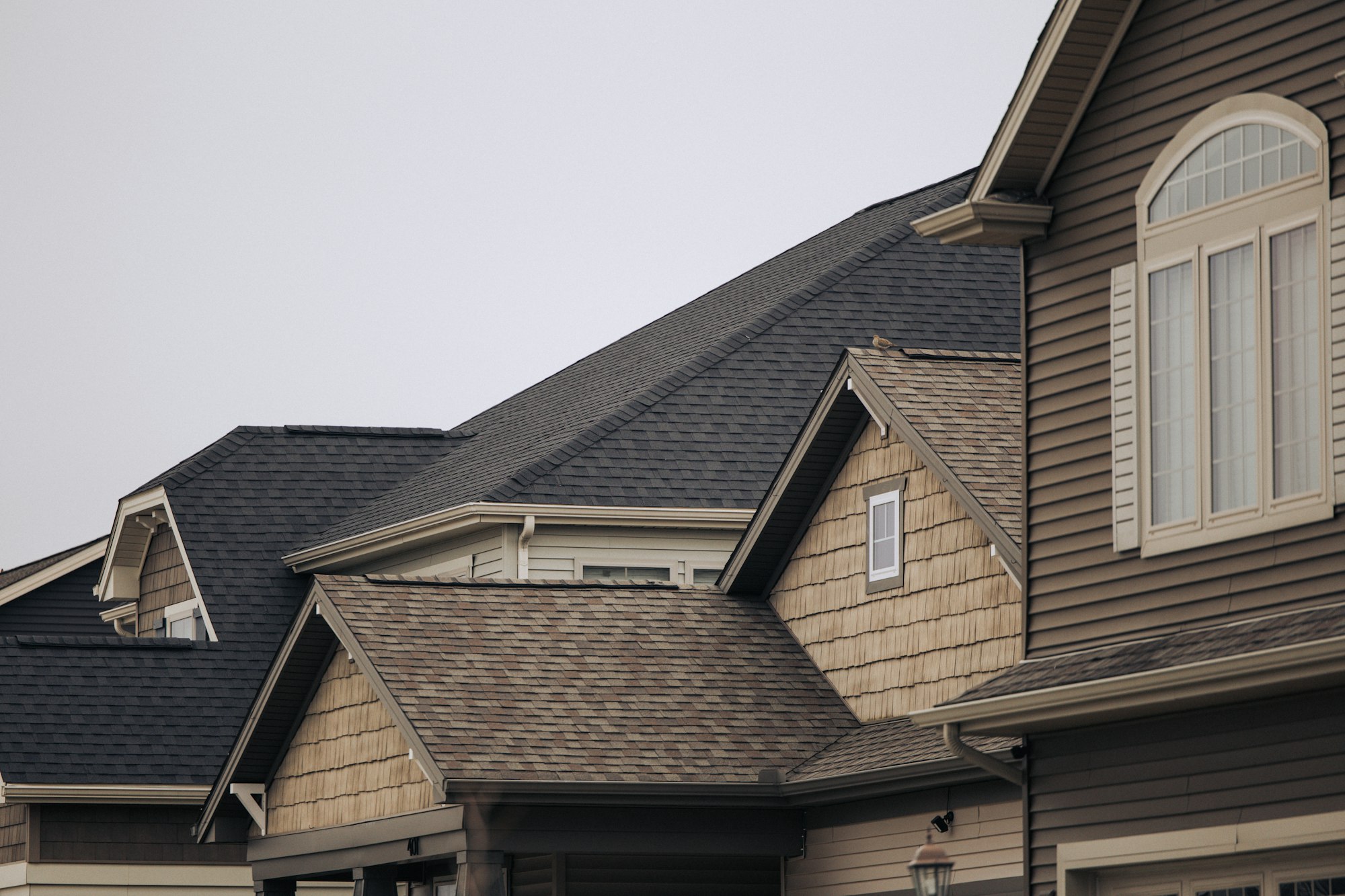 A row of suburban houses with grey asphalt shingle roofs, the kind of Plano, TX roof a manufacturer and workmanship warranty each cover in part.