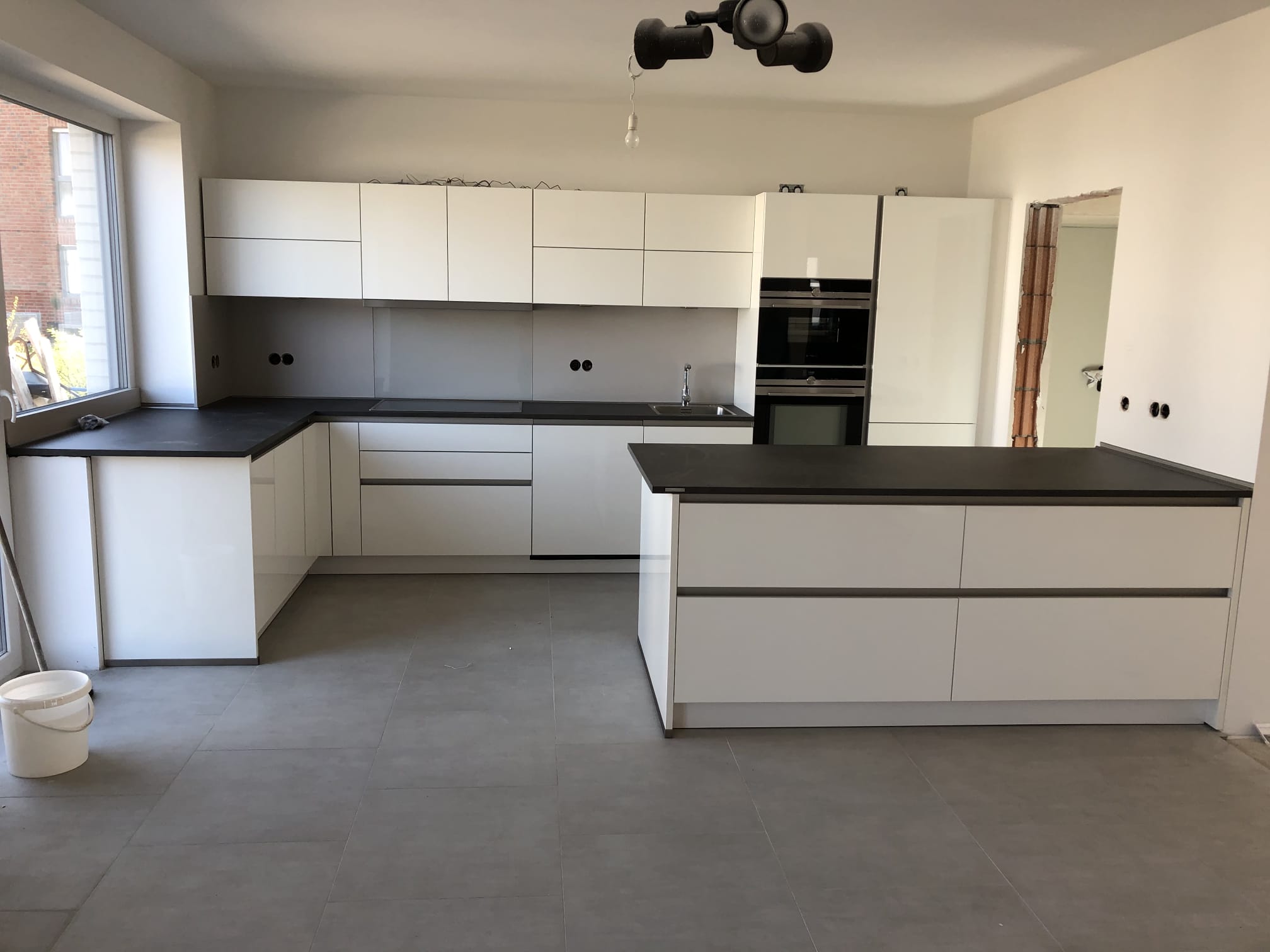 Weiße Einbauküche mit Halbinsel und dunkler Arbeitsplatte im Neubau