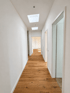 Heller Flur mit Holzboden, weißen Wänden und Dachfenstern in einer modernisierten Wohnung.